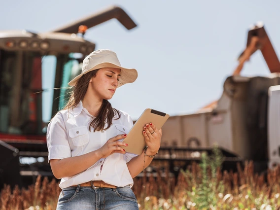 Person looking at a clipboard while standing in front of farm equipment in a field.