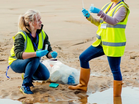 Two people testing water samples on a beach.